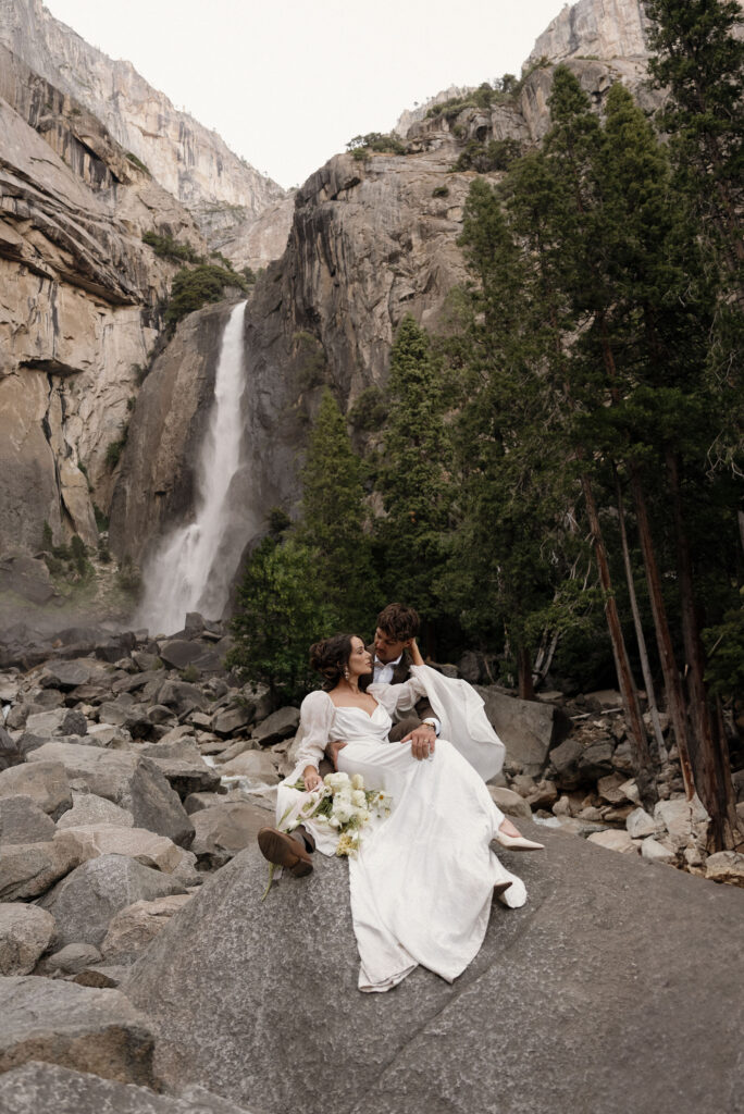 Intimate Yosemite elopement portrait of bride and groom seated on granite rocks