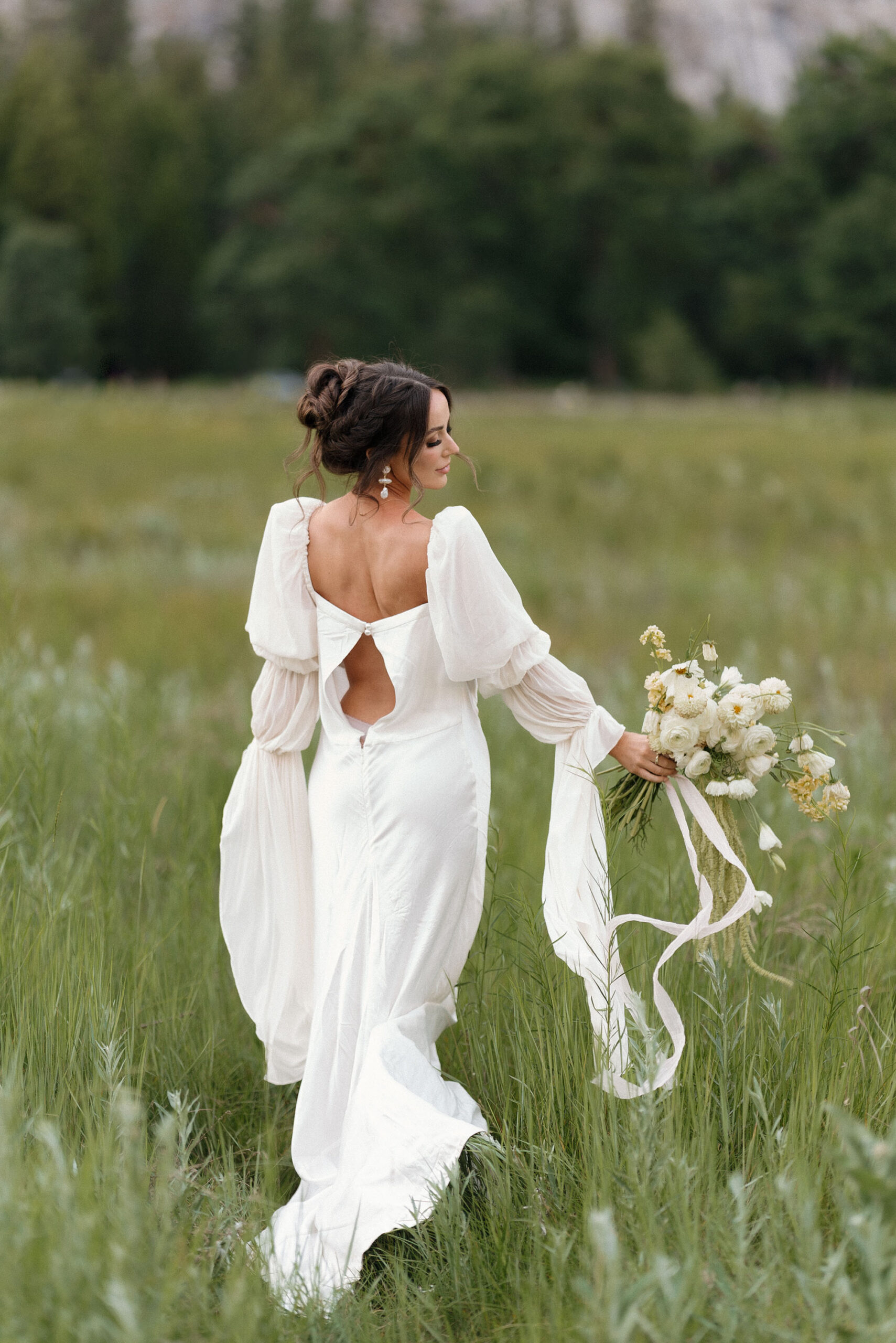 Bride standing in field with delicate button-back wedding dress