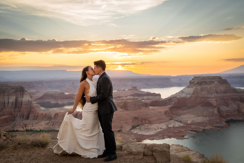 Bride and groom sharing a kiss with dramatic desert cliffs behind them.