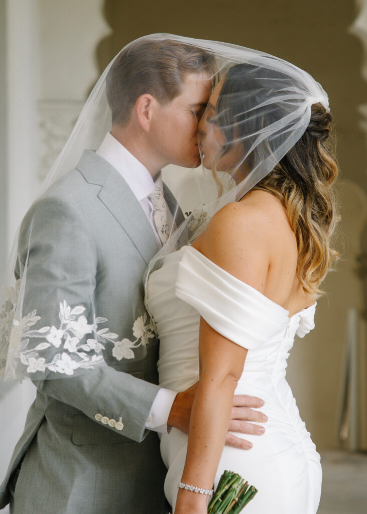 Groom kissing bride covered in wedding veil
