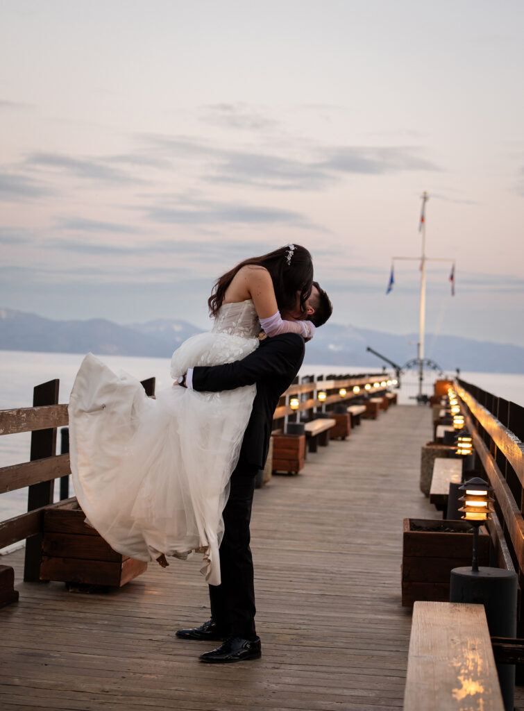 Groom lifting bride for a kiss on the dock at sunset