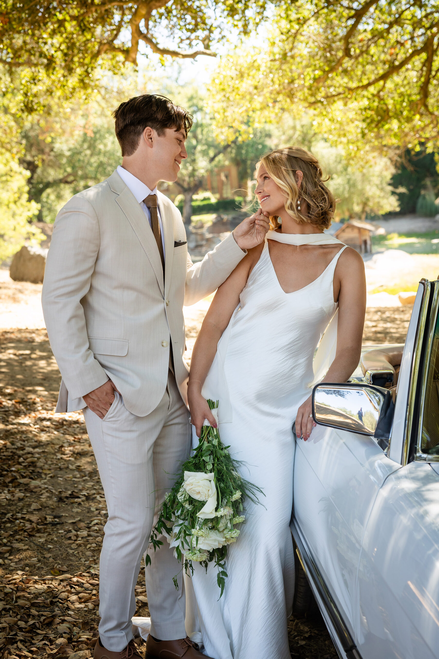 Groom staring lovingly at bride by their wedding car