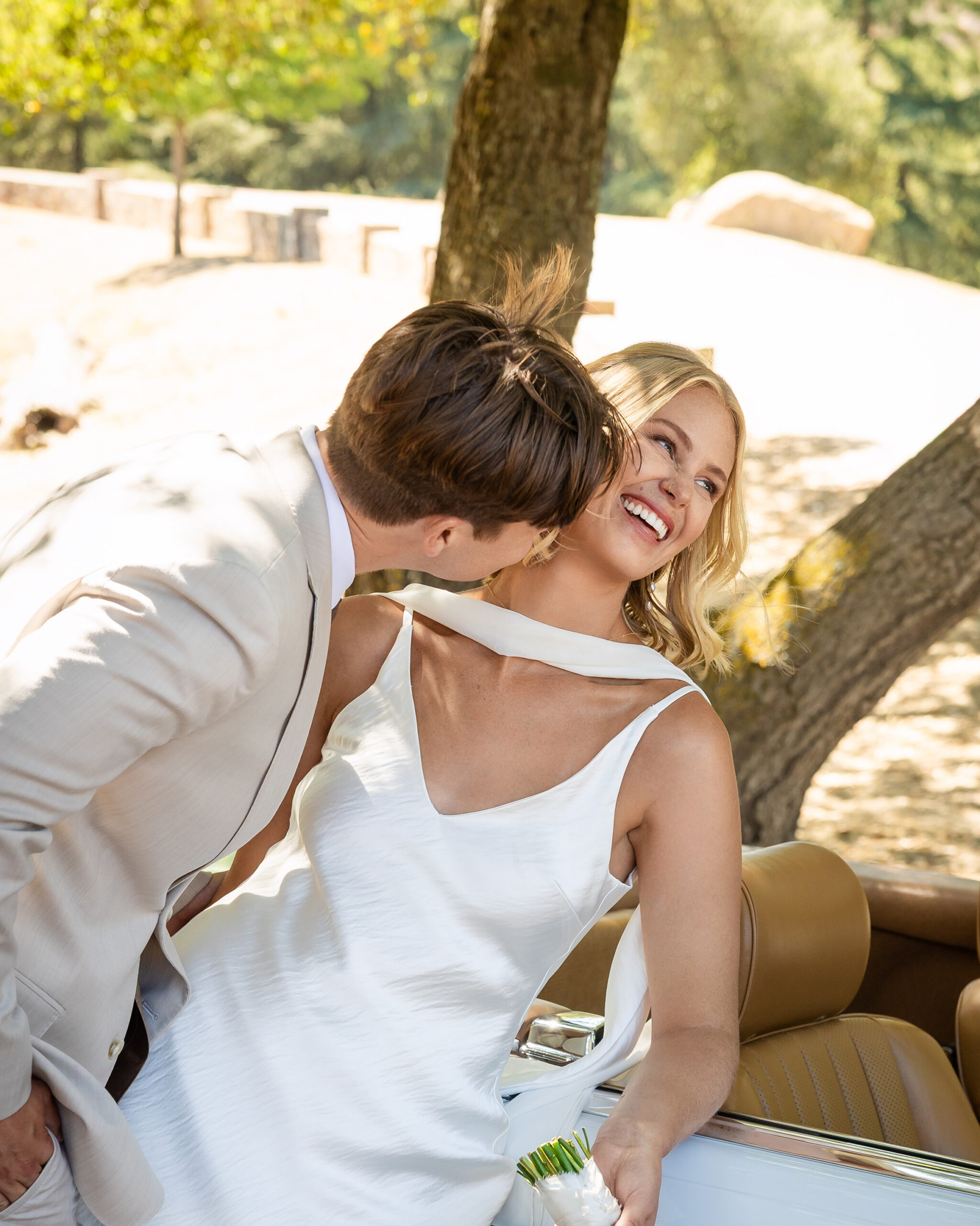 Groom kissing bride on the cheek beside a vintage bridal car