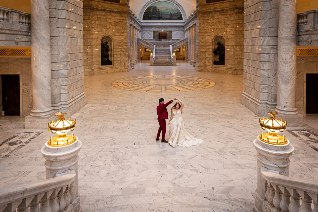 Bride laughing as the groom twirls her inside the marble halls of the Utah State Capitol — romantic Salt Lake City elopement.
