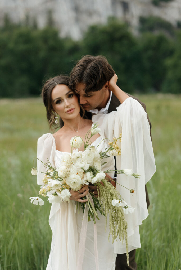 Newlyweds embracing in a wide open field surrounded by Yosemite mountains