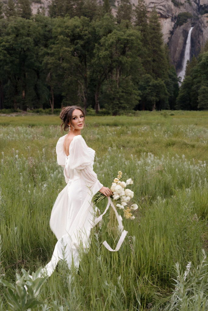 Bride standing in an open Yosemite field surrounded by golden grass and mountains